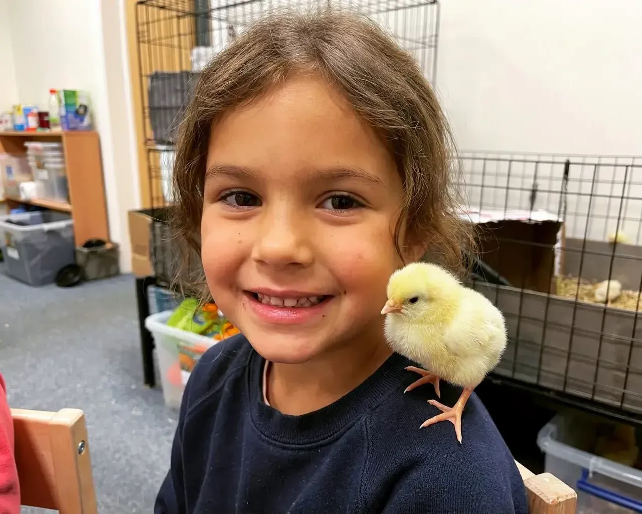 A smiling girl with a yellow chick perched on her shoulder